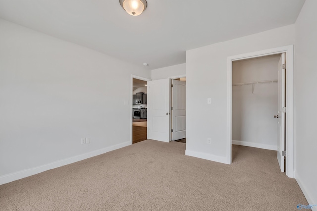 unfurnished bedroom with a spacious closet, baseboards, a closet, and light colored carpet