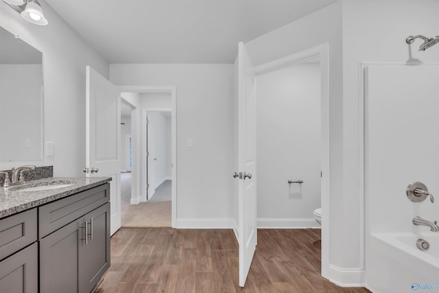 bathroom with shower / washtub combination, toilet, vanity, wood finished floors, and baseboards