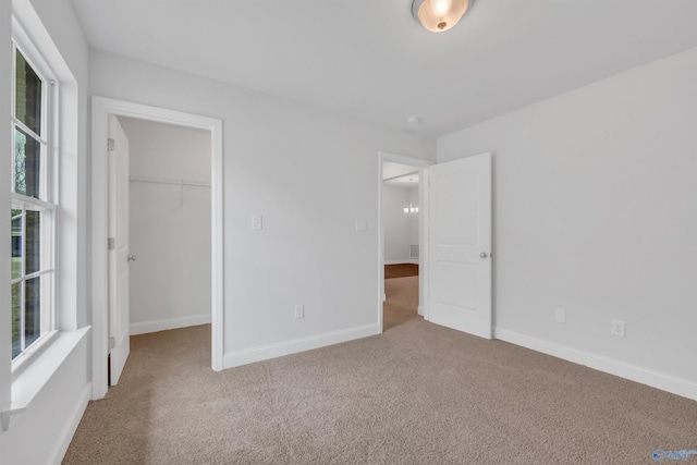 unfurnished bedroom with a walk in closet, multiple windows, light carpet, and baseboards