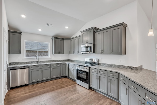 kitchen featuring stainless steel appliances, wood finished floors, a sink, hanging light fixtures, and gray cabinets