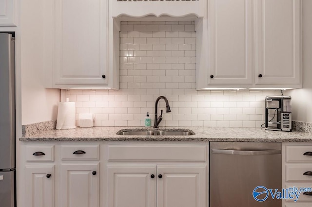 kitchen featuring white cabinets, sink, backsplash, stainless steel appliances, and light stone countertops