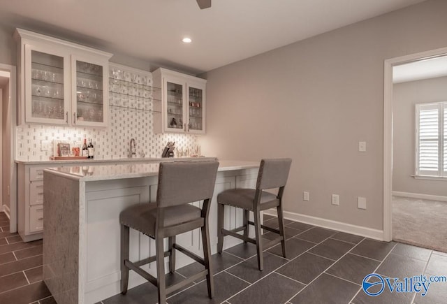 bar with dark tile patterned floors, white cabinetry, tasteful backsplash, and sink