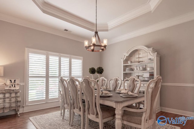 dining space featuring crown molding, a tray ceiling, an inviting chandelier, and dark wood-type flooring