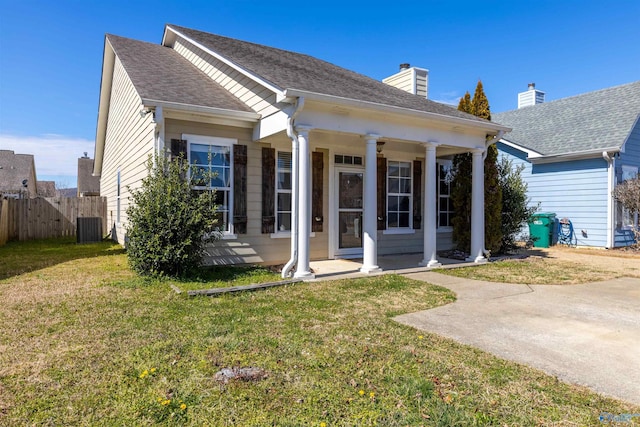 view of front of house featuring a porch, fence, a front yard, a shingled roof, and central AC unit