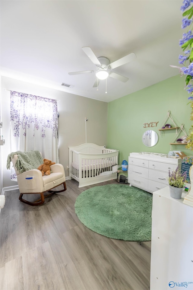 bedroom featuring a ceiling fan, visible vents, baseboards, a nursery area, and light wood-style floors