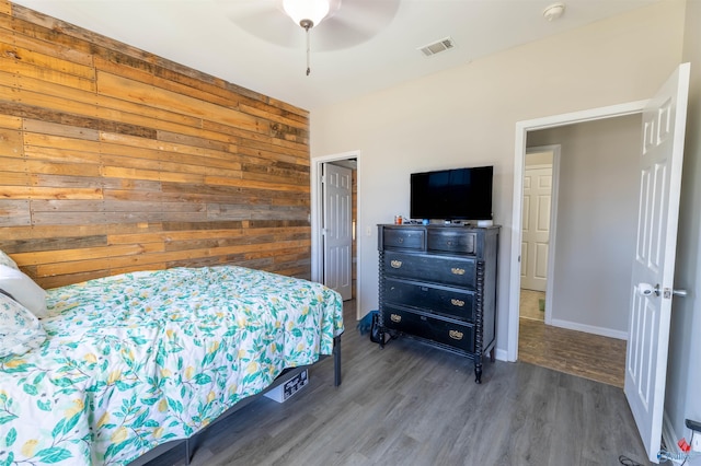 bedroom with wood finished floors, visible vents, wood walls, and ceiling fan