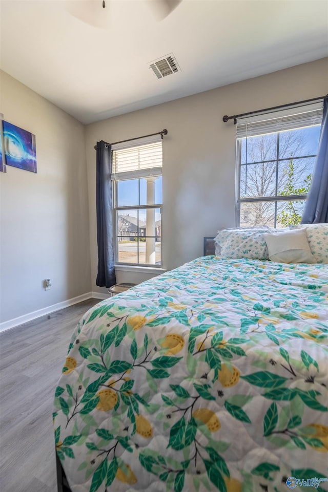 bedroom featuring wood finished floors, multiple windows, baseboards, and visible vents