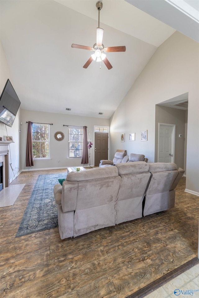 living area with a ceiling fan, wood finished floors, baseboards, high vaulted ceiling, and a fireplace with flush hearth