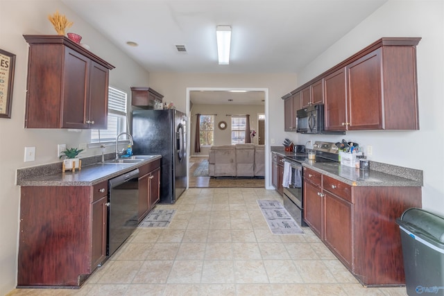 kitchen featuring visible vents, black appliances, a sink, dark countertops, and reddish brown cabinets