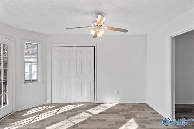 unfurnished bedroom with ceiling fan, a textured ceiling, light wood-type flooring, and a closet