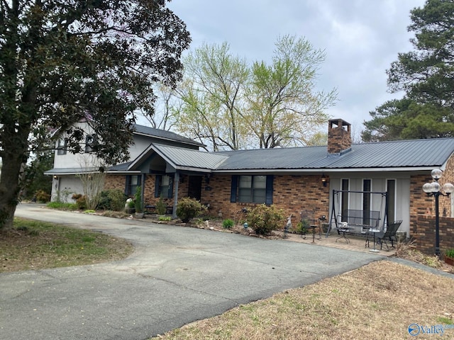 view of front of house with a chimney, driveway, metal roof, and brick siding