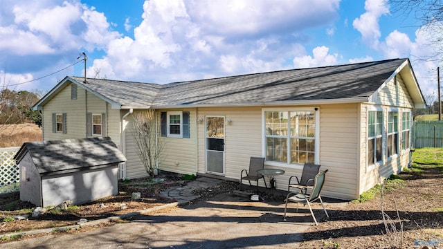 rear view of house with a patio, an outdoor structure, and a shingled roof