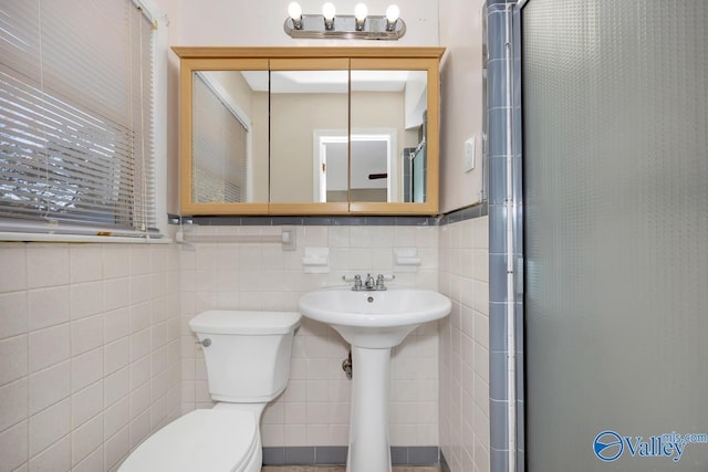 bathroom featuring a shower with door, toilet, tile walls, and sink