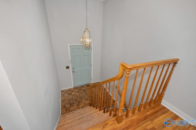 stairs featuring wood-type flooring and an inviting chandelier