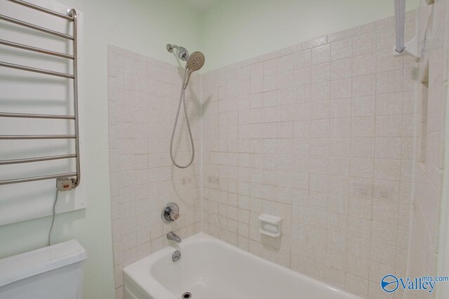 bathroom with tiled shower / bath, radiator heating unit, and toilet