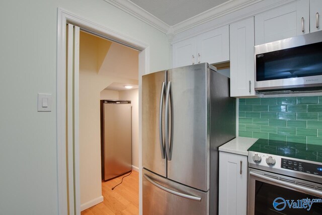 kitchen featuring tasteful backsplash, ornamental molding, appliances with stainless steel finishes, and white cabinets