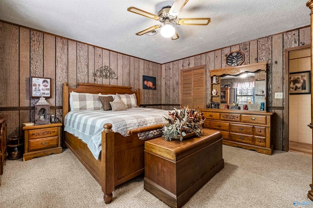 bedroom featuring a textured ceiling, wood walls, ceiling fan, and light colored carpet