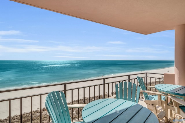 balcony with outdoor dining area, a water view, and a view of the beach