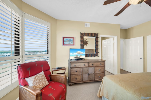 bedroom featuring a ceiling fan, light carpet, visible vents, and a textured ceiling