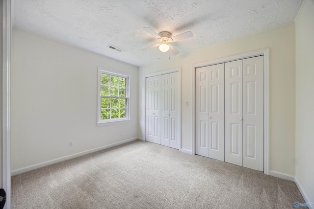 unfurnished bedroom with carpet flooring, a textured ceiling, two closets, and baseboards