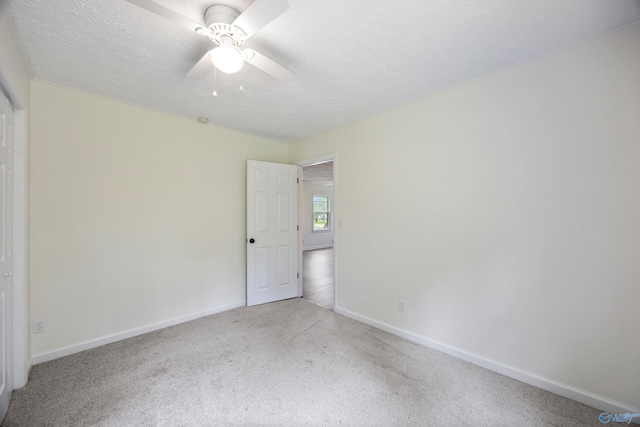 carpeted spare room featuring a textured ceiling, ceiling fan, and baseboards