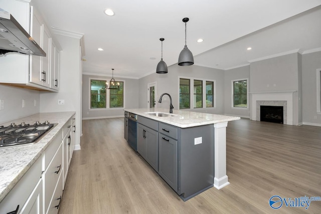 kitchen with an island with sink, sink, white cabinets, hanging light fixtures, and wall chimney exhaust hood