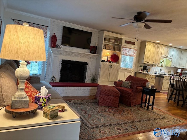 living room with crown molding, ceiling fan, wood-type flooring, and a fireplace