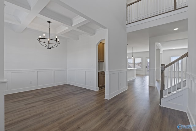 unfurnished dining area with stairs, beamed ceiling, dark wood finished floors, and arched walkways