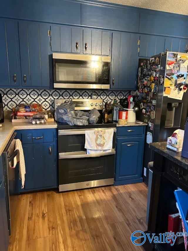 kitchen featuring blue cabinetry, tasteful backsplash, light countertops, appliances with stainless steel finishes, and wood finished floors