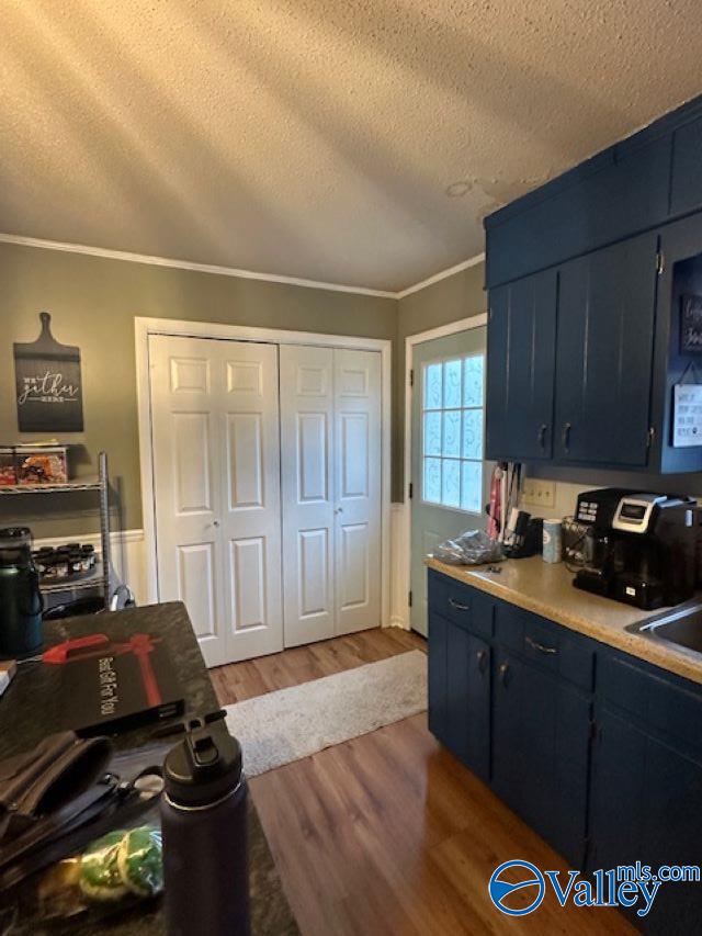 kitchen featuring crown molding, light countertops, a textured ceiling, wood finished floors, and blue cabinets