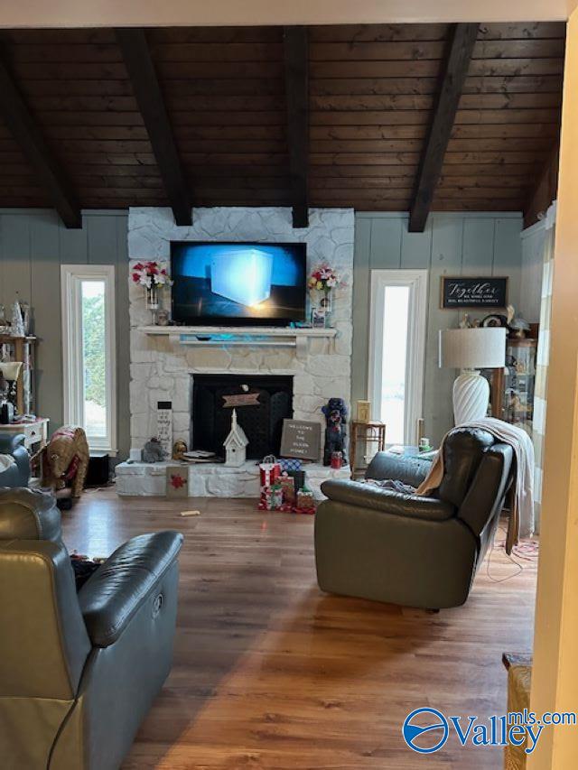 living room with lofted ceiling with beams, wood ceiling, wood finished floors, and a stone fireplace