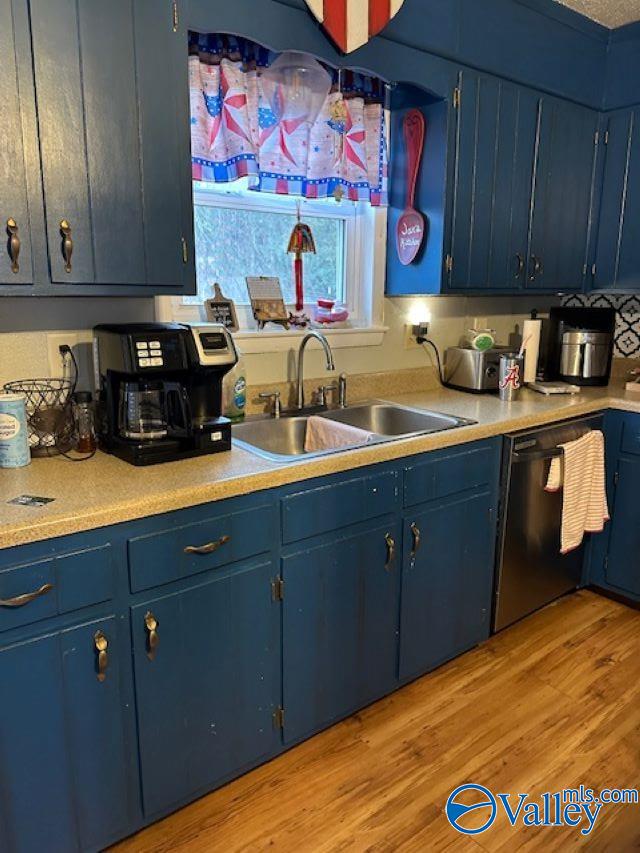 kitchen featuring light wood finished floors, dishwasher, blue cabinets, light countertops, and a sink