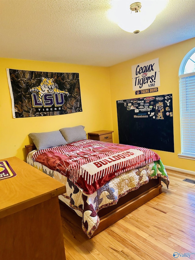 bedroom featuring wood finished floors, visible vents, and a textured ceiling