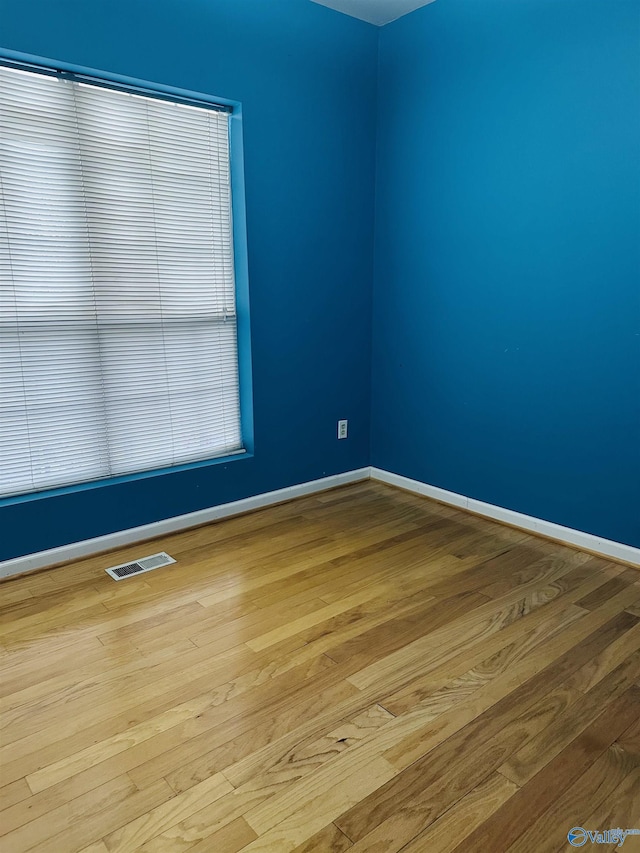 spare room with wood finished floors, visible vents, and baseboards