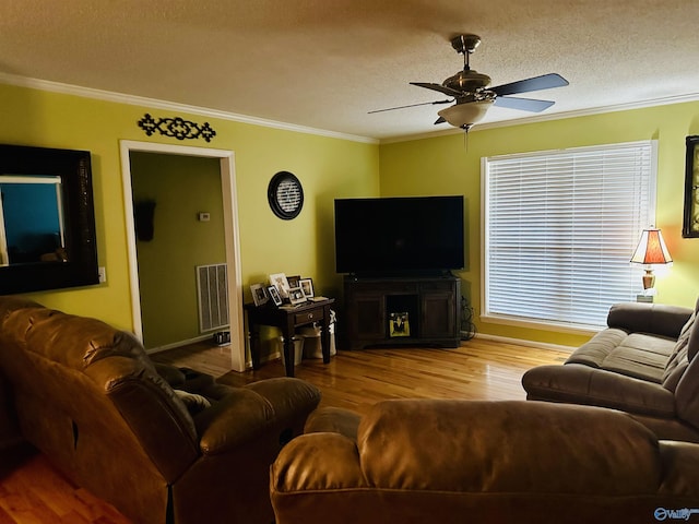 living area featuring wood finished floors, visible vents, ceiling fan, a textured ceiling, and crown molding