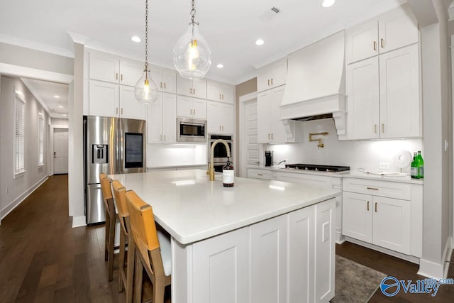 kitchen featuring a kitchen island with sink, appliances with stainless steel finishes, white cabinets, and premium range hood