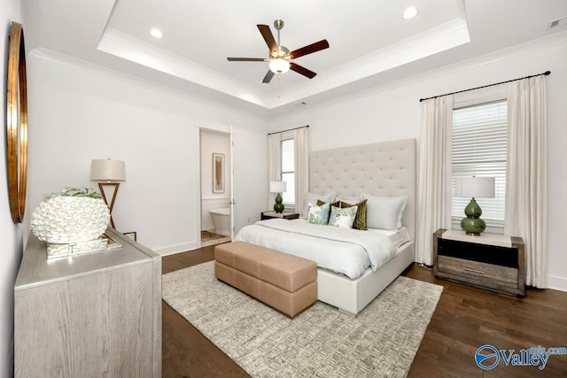 bedroom with crown molding, connected bathroom, dark hardwood / wood-style flooring, and a raised ceiling