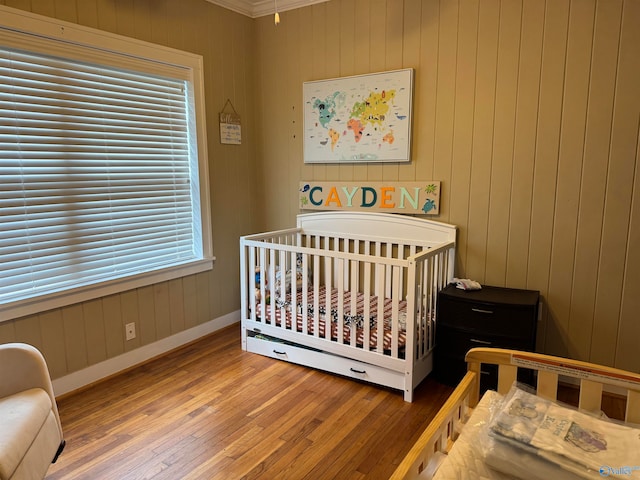 bedroom featuring hardwood / wood-style flooring, wood walls, a crib, and crown molding