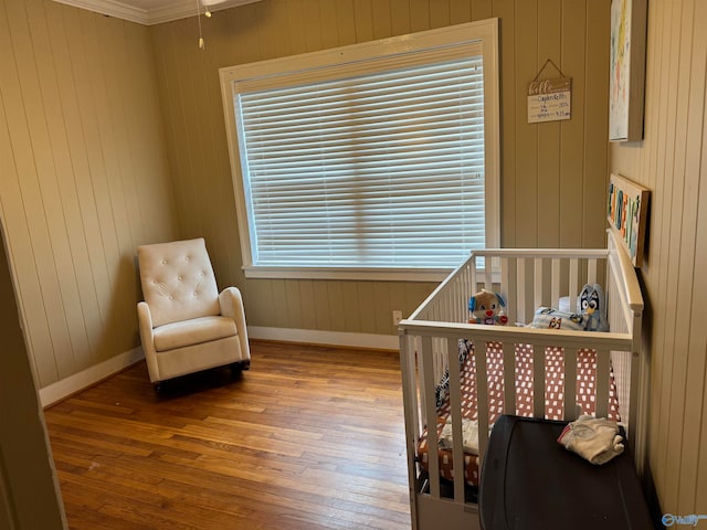 bedroom with a crib, wood-type flooring, multiple windows, and ornamental molding