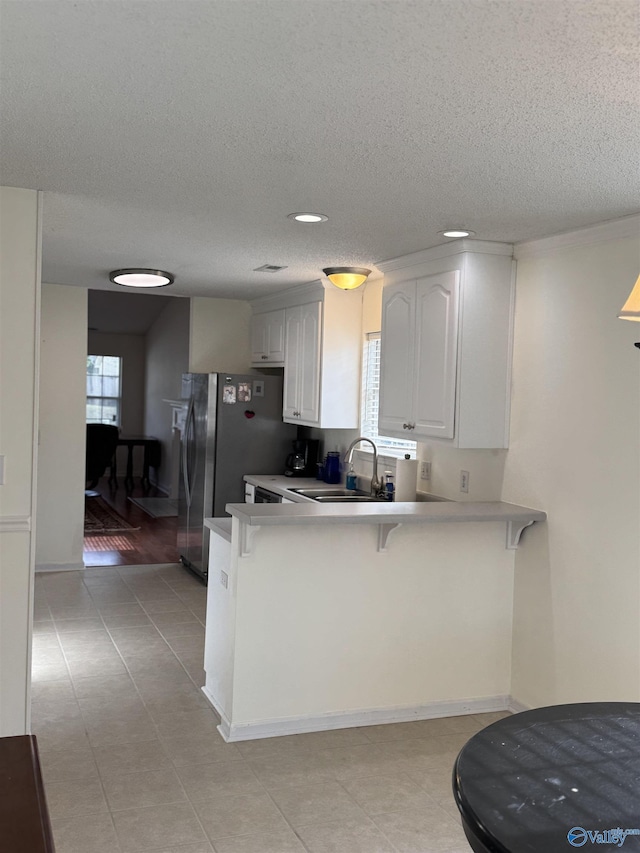 kitchen featuring a breakfast bar area, a textured ceiling, a sink, a peninsula, and white cabinetry