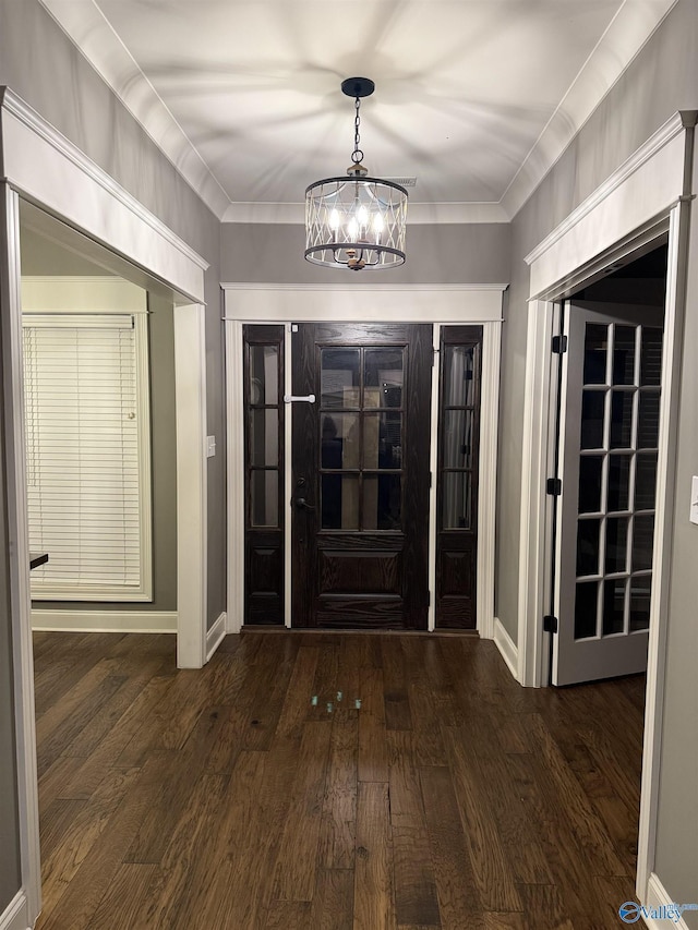 foyer entrance featuring dark wood-type flooring, ornamental molding, and a chandelier