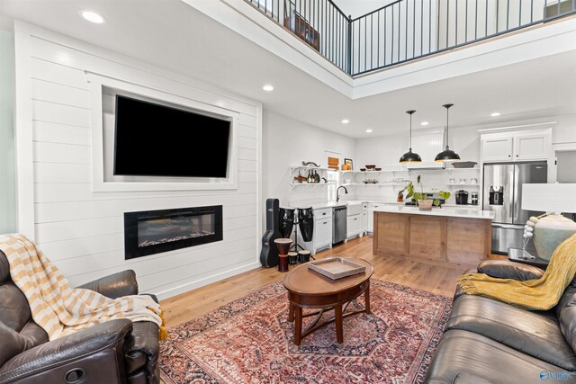 living room featuring sink, light wood-type flooring, and a towering ceiling