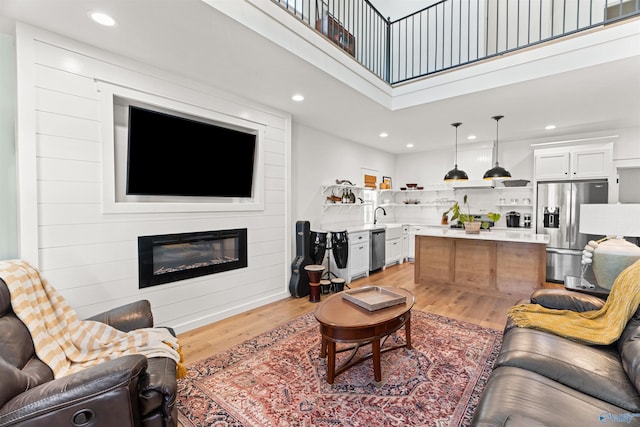 living room with a fireplace, recessed lighting, light wood-type flooring, and a towering ceiling