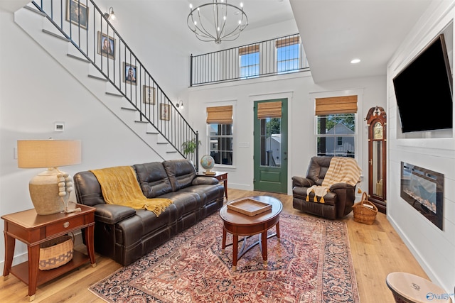 living room with wood finished floors, recessed lighting, stairs, a glass covered fireplace, and a notable chandelier