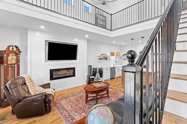 living area with light wood-style flooring, a fireplace, stairs, and a towering ceiling