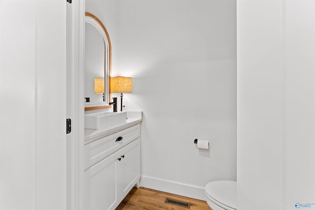half bath with vanity, wood finished floors, visible vents, baseboards, and toilet