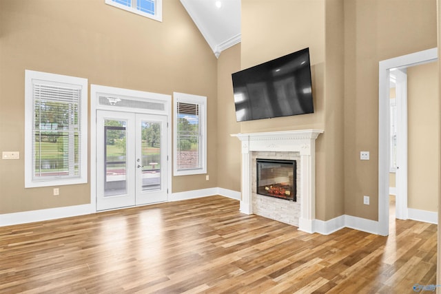 unfurnished living room featuring crown molding, high vaulted ceiling, a glass covered fireplace, baseboards, and wood finished floors