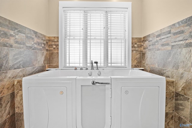 clothes washing area featuring a healthy amount of sunlight, tile walls, and laundry area