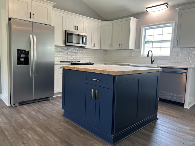 kitchen with a kitchen island, white cabinets, vaulted ceiling, appliances with stainless steel finishes, and dark wood finished floors