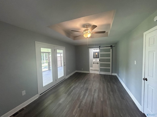 spare room with ceiling fan, a barn door, dark wood-style flooring, baseboards, and a raised ceiling